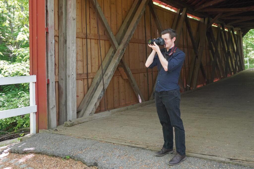 Real Estate Photographer Wesley Ward points a camera away from a red covered bridge.