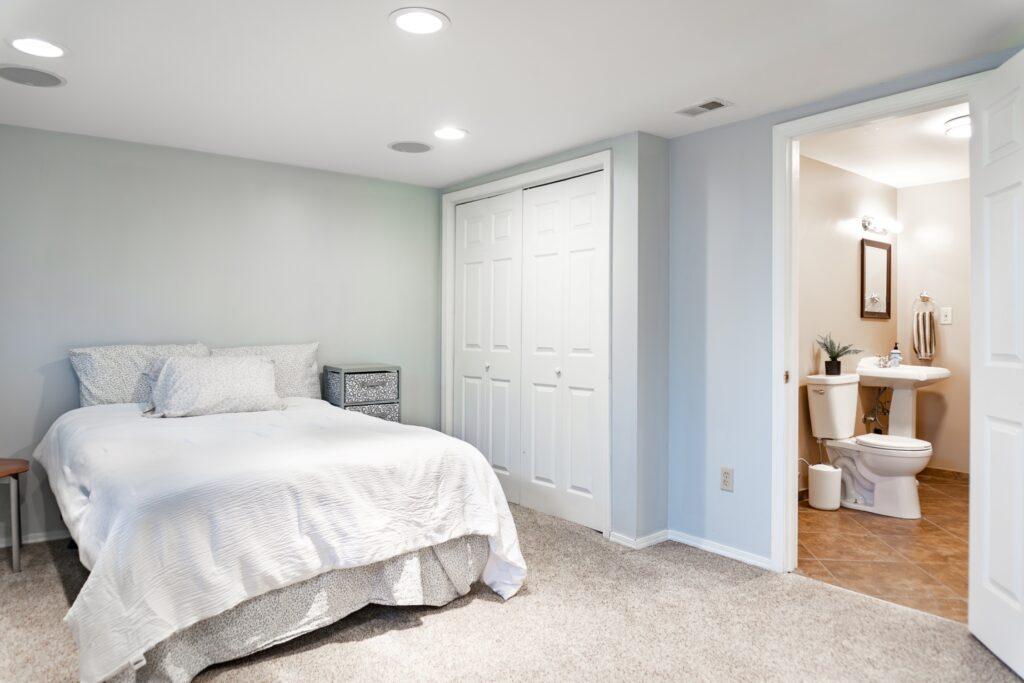 Guest bedroom with white bed, closet doors, and bathroom entry