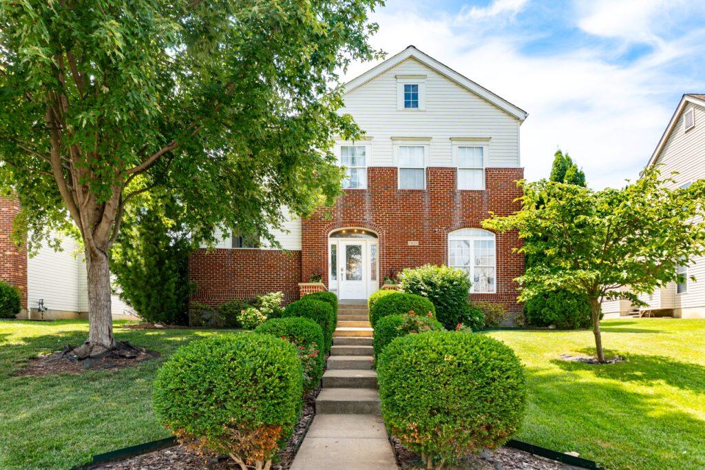 Front walkway with trimmed hedges leading to brick home