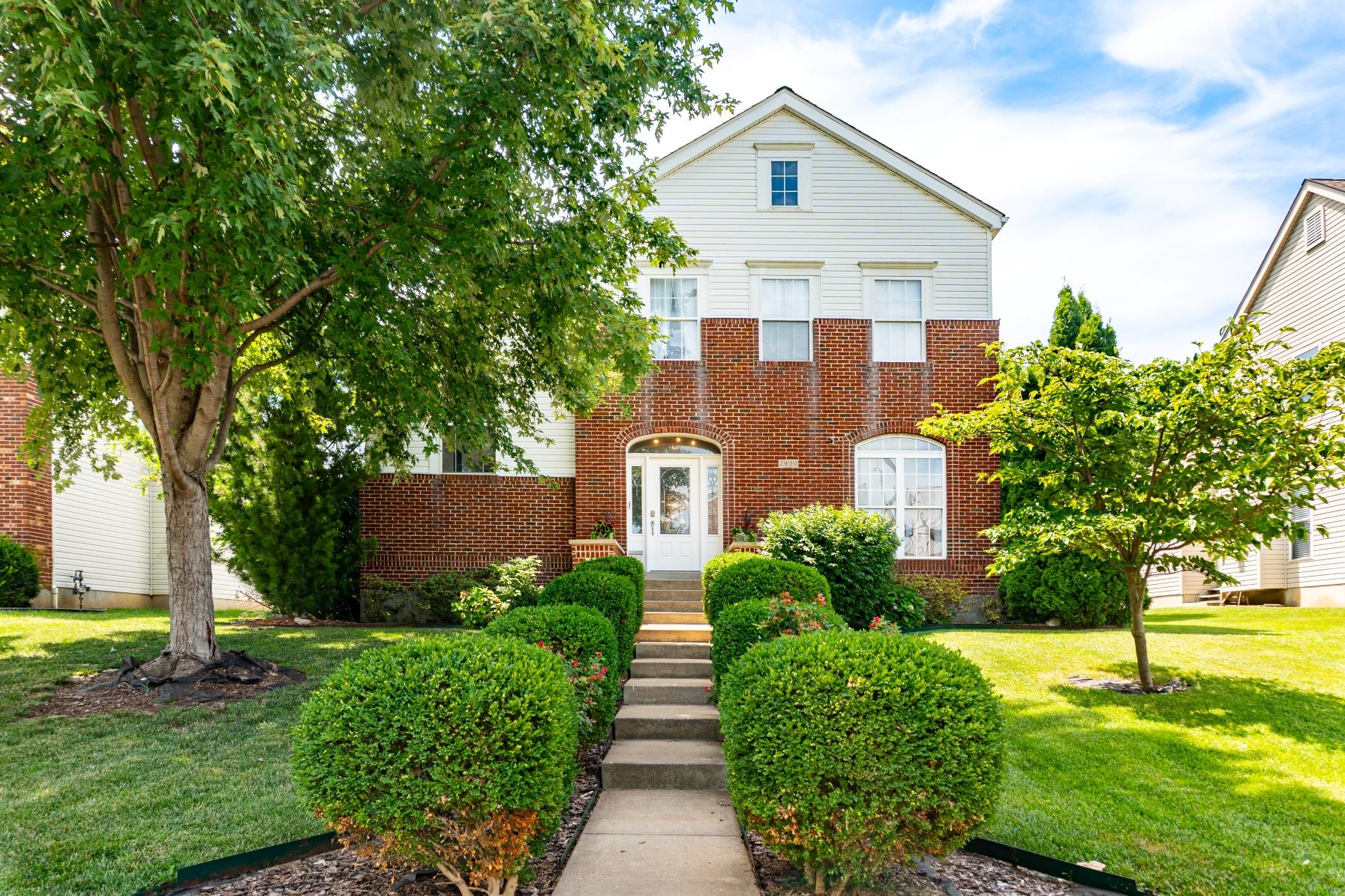 Front walkway with trimmed hedges leading to brick home