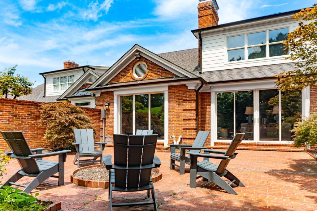 Backyard of a brick home with a firepit and black Adirondack chairs all around