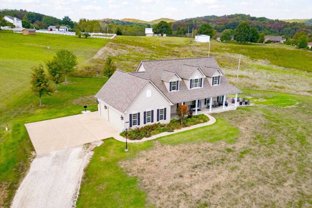 Aerial view of farmhouse with wraparound porch and open fields
