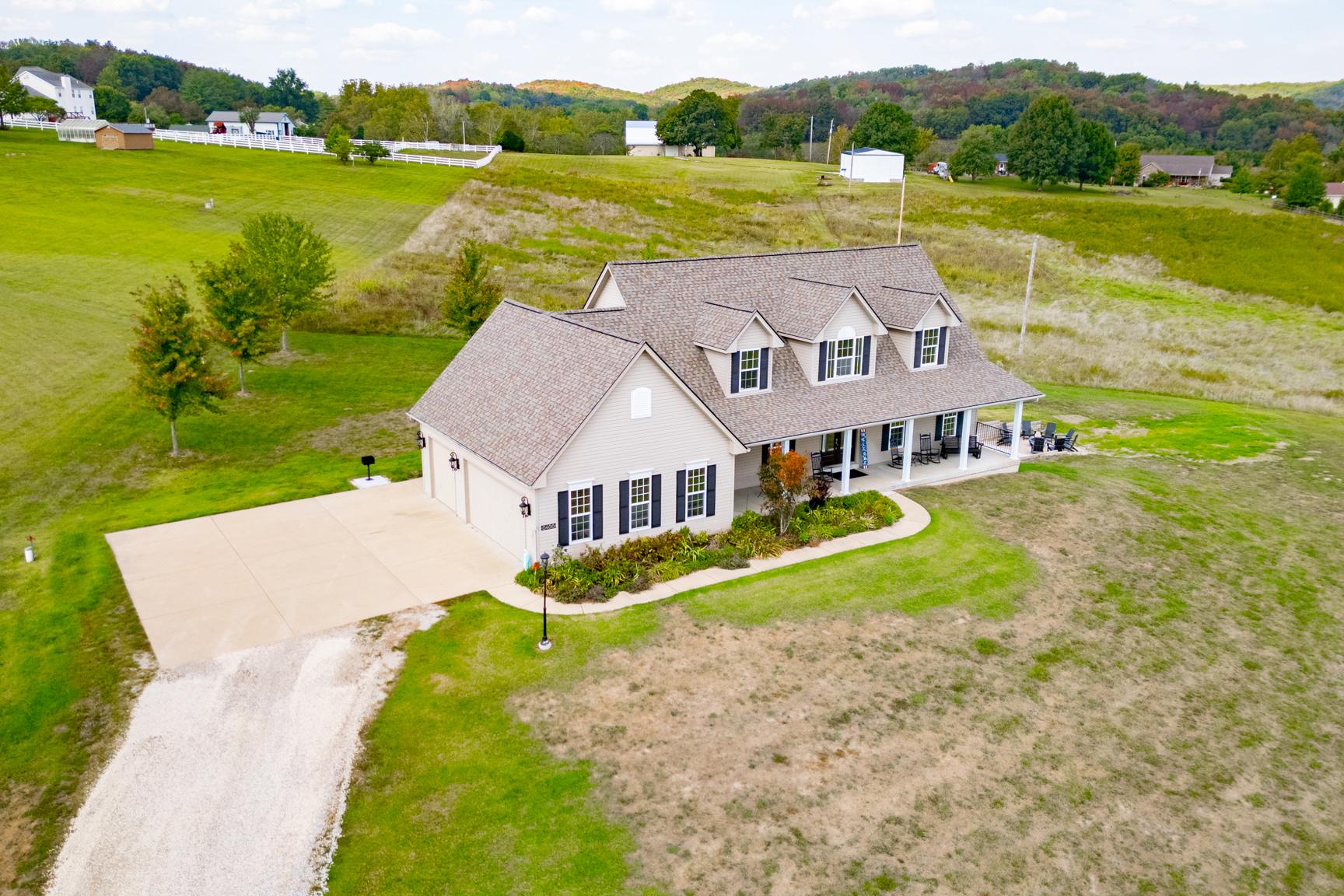Aerial view of farmhouse with wraparound porch and open fields