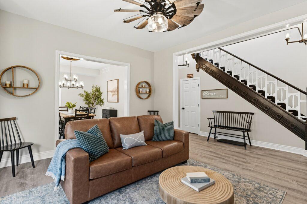 Living room with leather sofa, round coffee table, and staircase in background