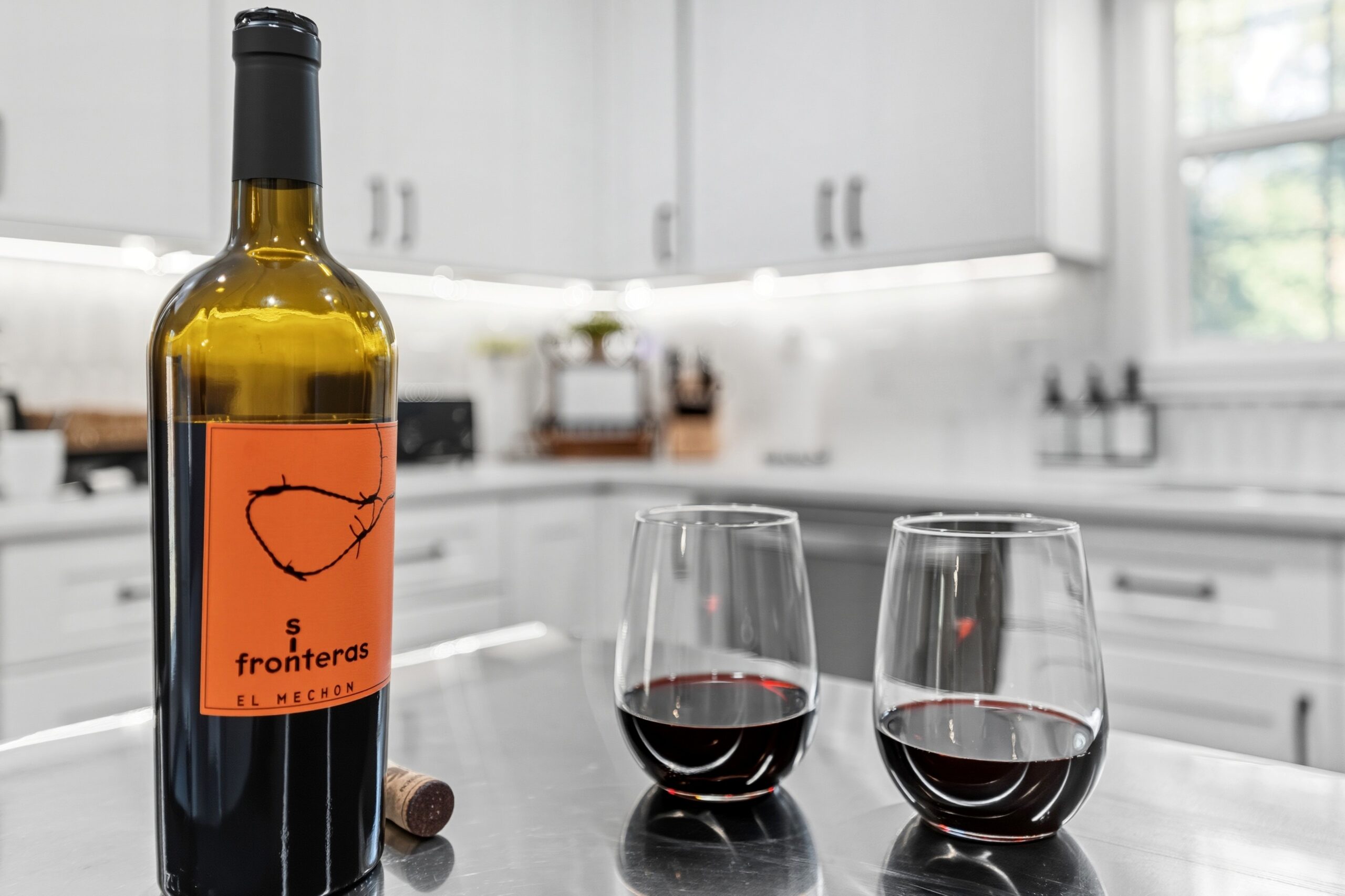 Bottle of wine and two glasses on kitchen counter with white cabinets in background