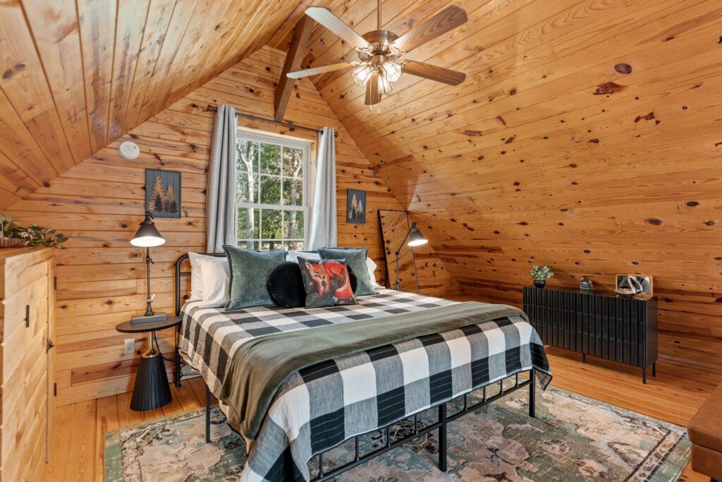Loft bedroom in log cabin with wood walls and ceiling fan