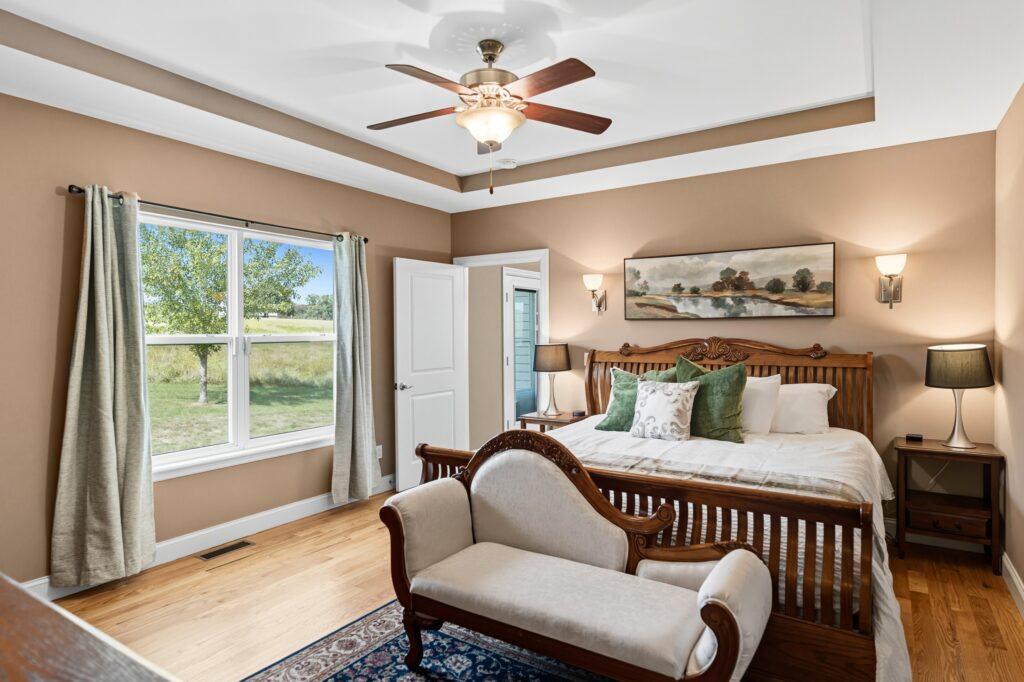 Primary bedroom with tray ceiling, ceiling fan, and sitting area