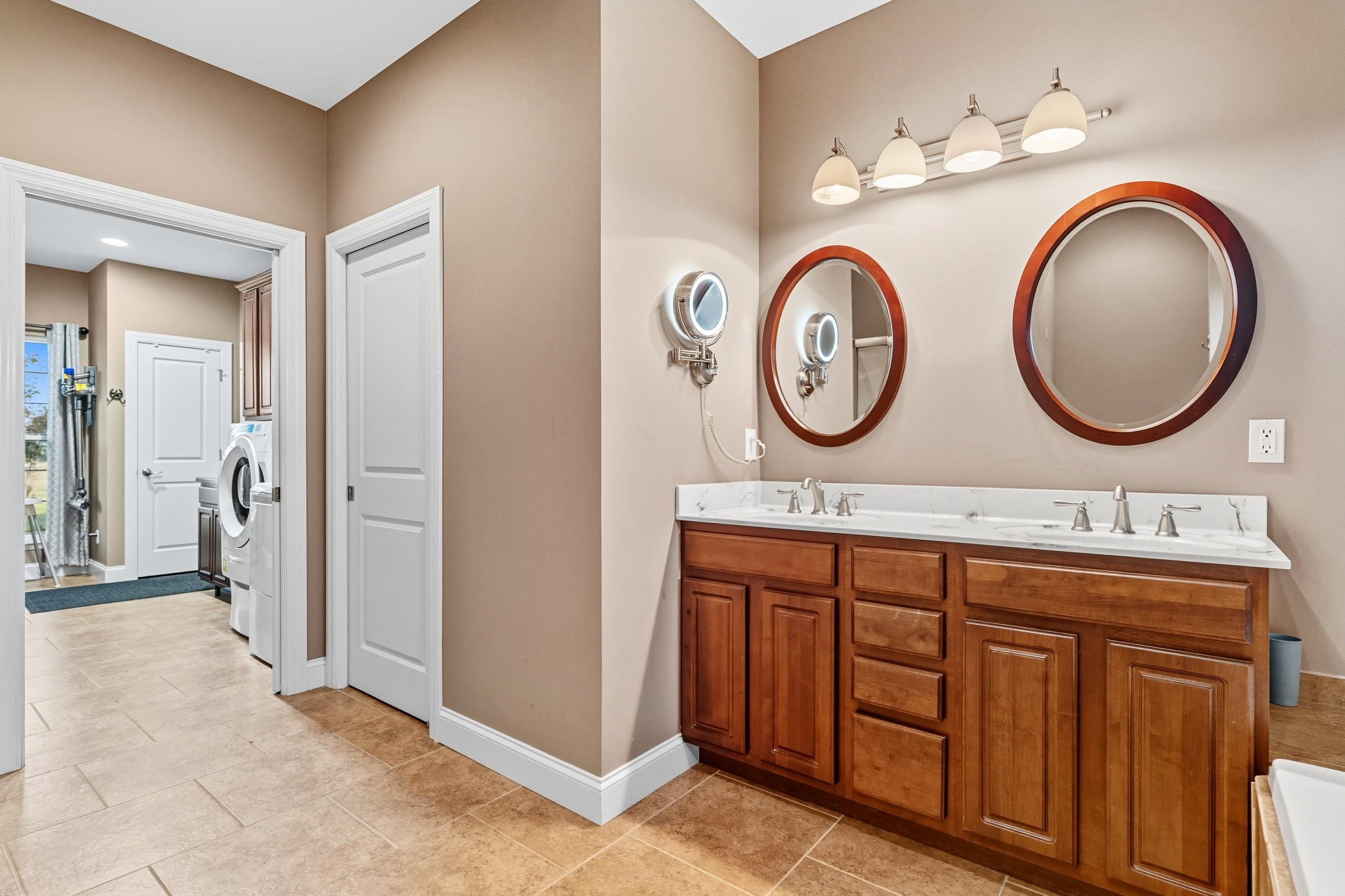 Bathroom with double vanity, wood cabinets, and round mirrors