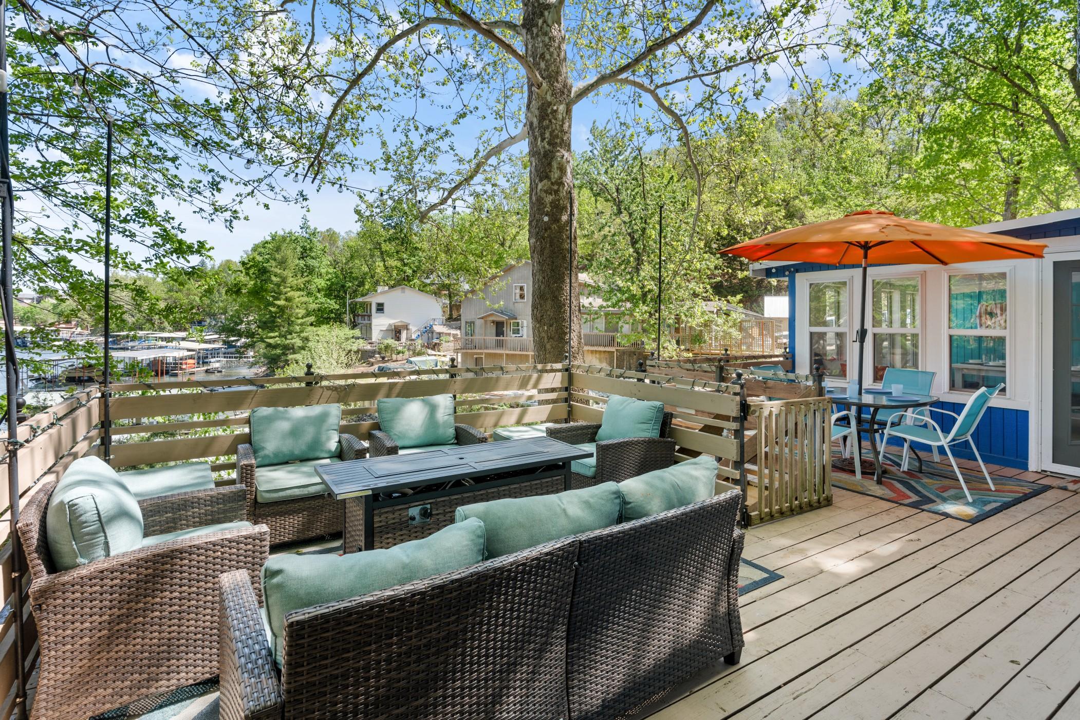 Porch with multiple outdoor couches, chairs, tables, and a fire pit all surrounded by trees