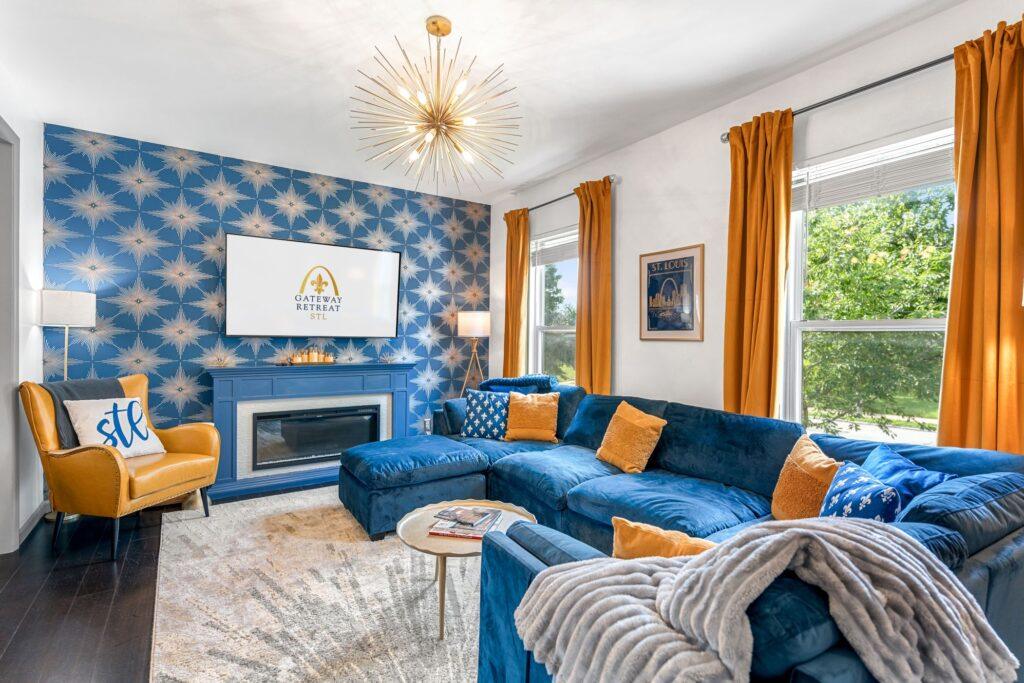 A living room with a large blue sectional and a TV mounted above a fire place.