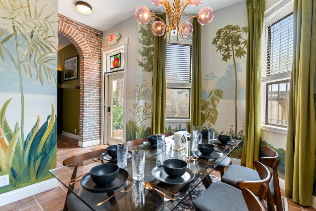 A dining room with wide windows, decorative wallpaper, and set glass table