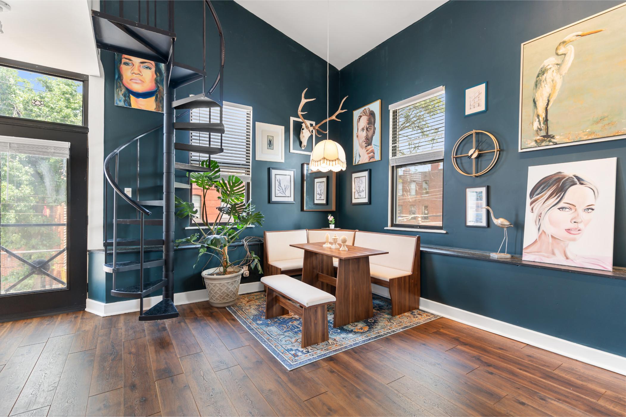 A living space with a corner couch and coffee table flanked by a spiral staircase with various works of art adorning the walls