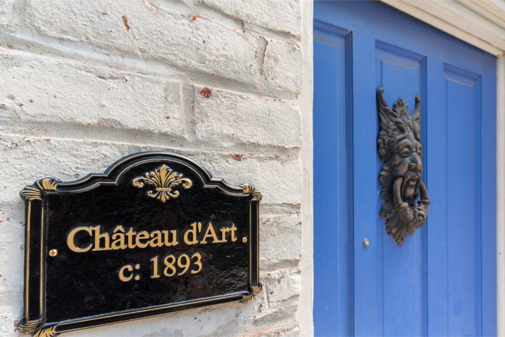 A close up shot of a plaque reading "Chateau d'Art c. 1893" with a blue door featuring a vintage knocker in the background