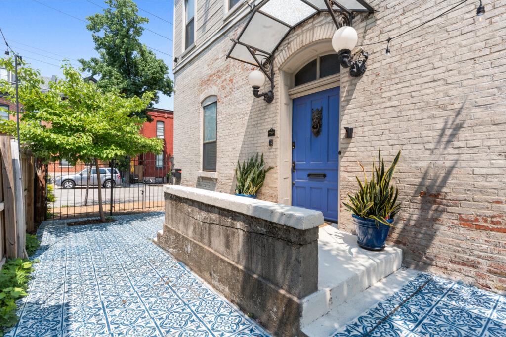 Exterior shot of a white brick building with a blue tile front patio and wrought iron fence