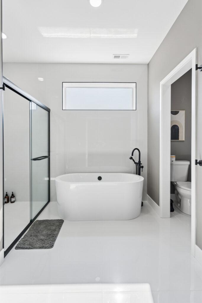 A bright white bathroom with a walk in shower on the left, bath tub in the center, and toilet on the right