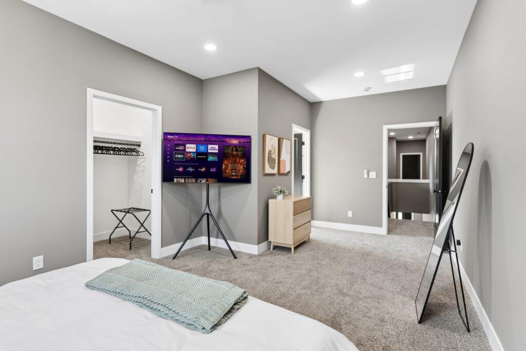 A bedroom with a TV mounted on a stand and a tall mirror leaning against the right-hand wall
