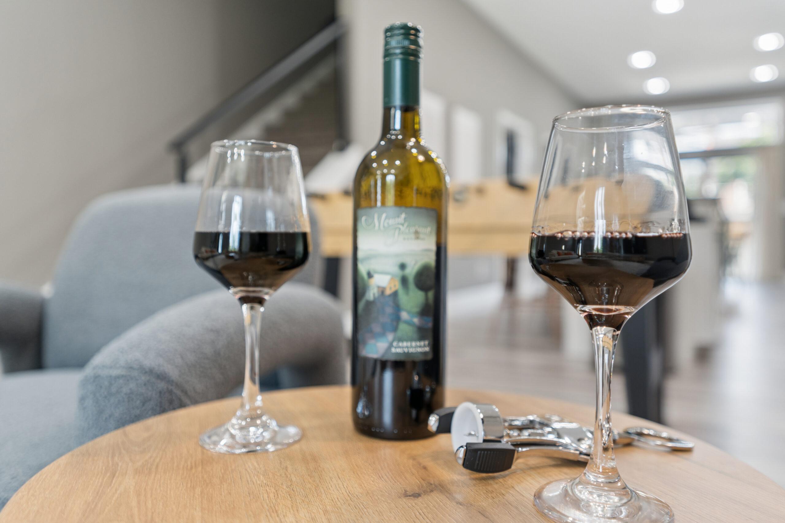 Close up of two half-full wine glasses, a bottle of wine, and a wine opener resting on a side table